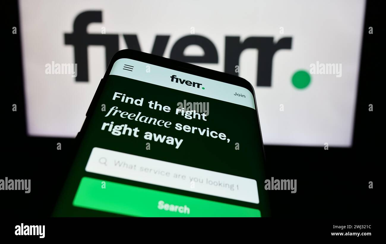 Mobile phone with website of freelance platform company Fiverr International Ltd. in front of business logo. Focus on top-left of phone display. Stock Photo