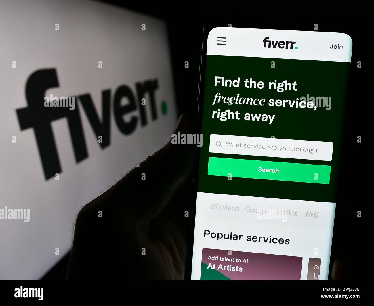 Person holding cellphone with webpage of freelance platform company Fiverr International Ltd. in front of logo. Focus on center of phone display. Stock Photo