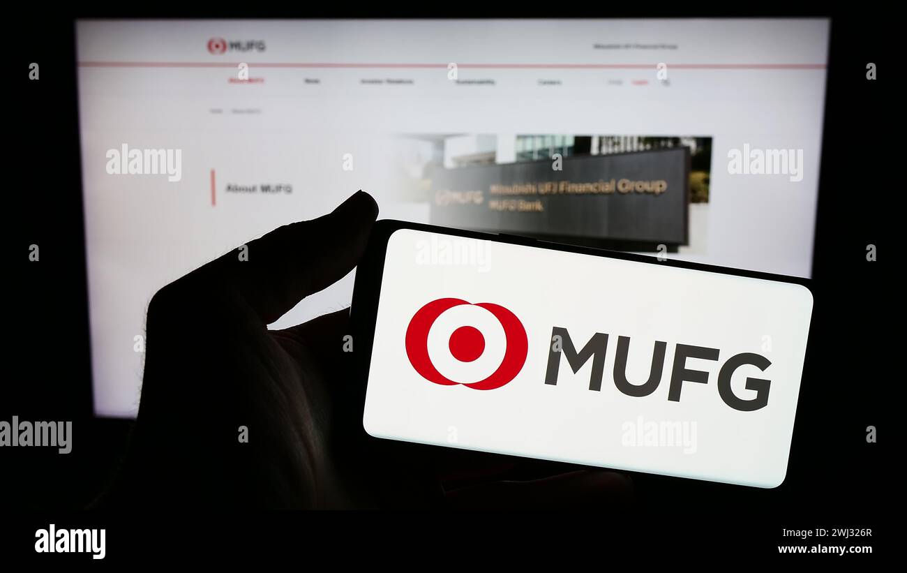 Person holding smartphone with logo of company Mitsubishi UFJ Financial Group Inc. (MUFG) in front of website. Focus on phone display. Stock Photo