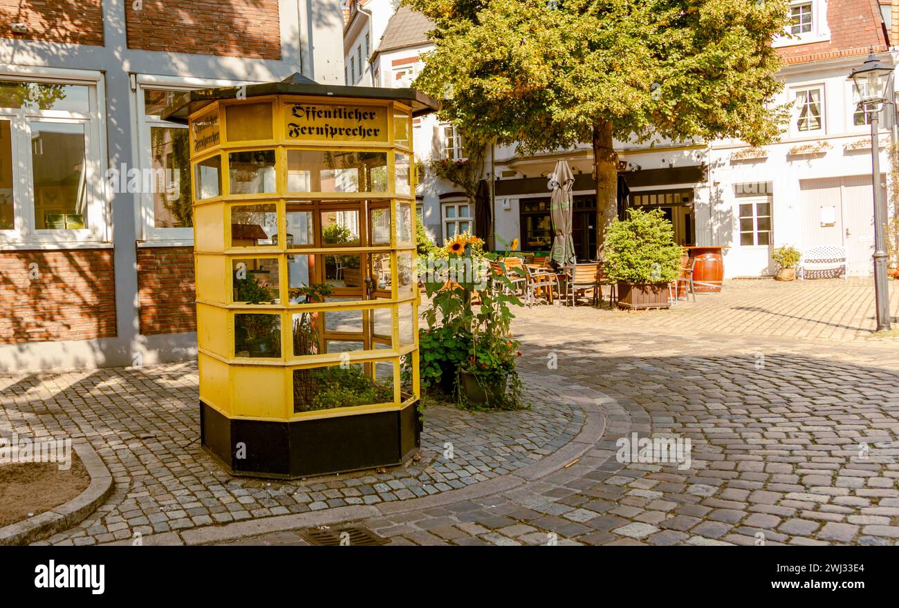 Traditional German telephone box with flowers. Old yellow telephone booth in Germany with text Ã¶ffen Stock Photo