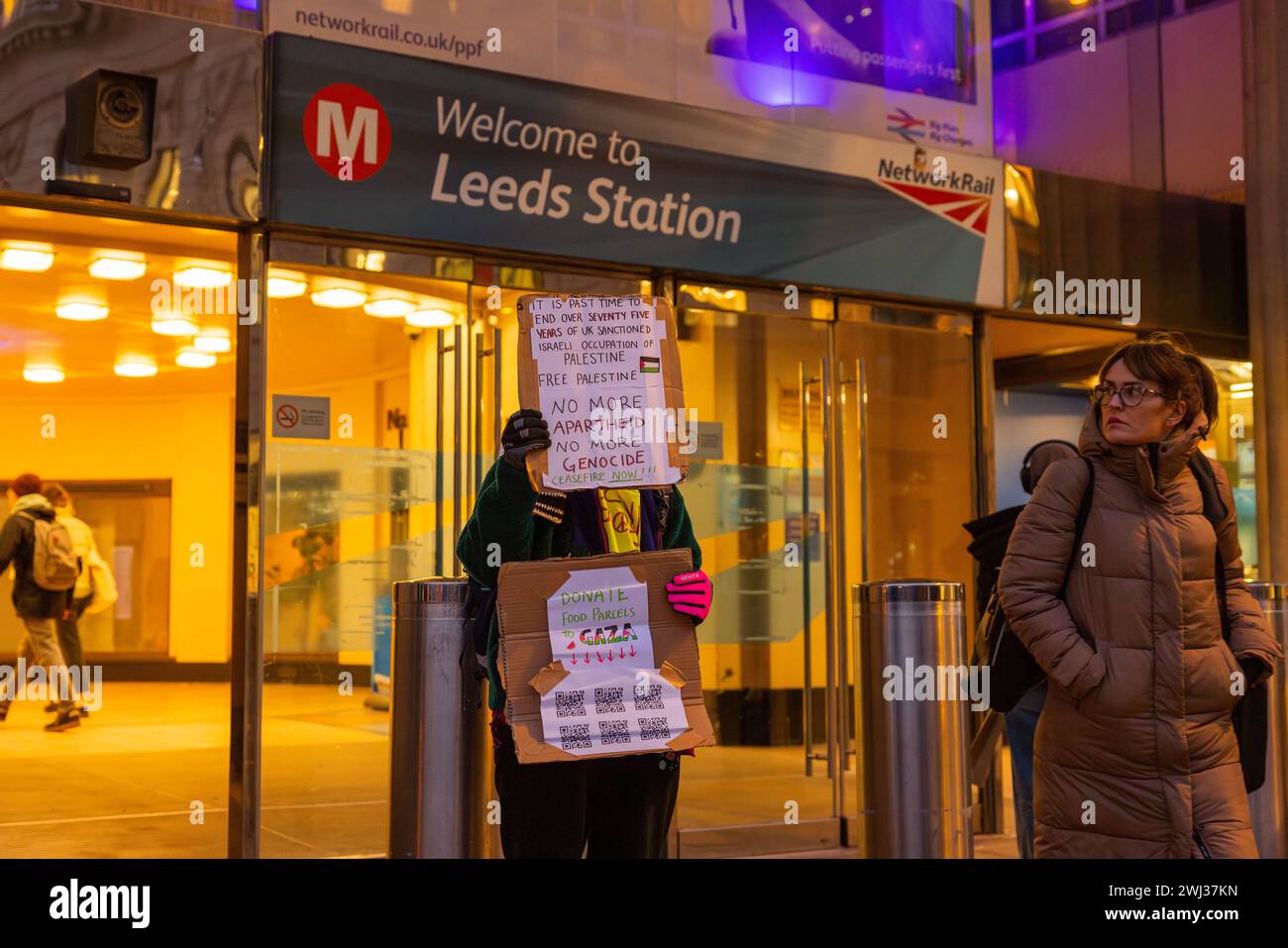 Leeds, UK. 12 FEB, 2024. Protestor holds 'no more aparthied no more genocide banner' outside the entryway to Leeds train station. Credit Milo Chandler/Alamy Live News. Credit Milo Chandler/Alamy Live News Stock Photo