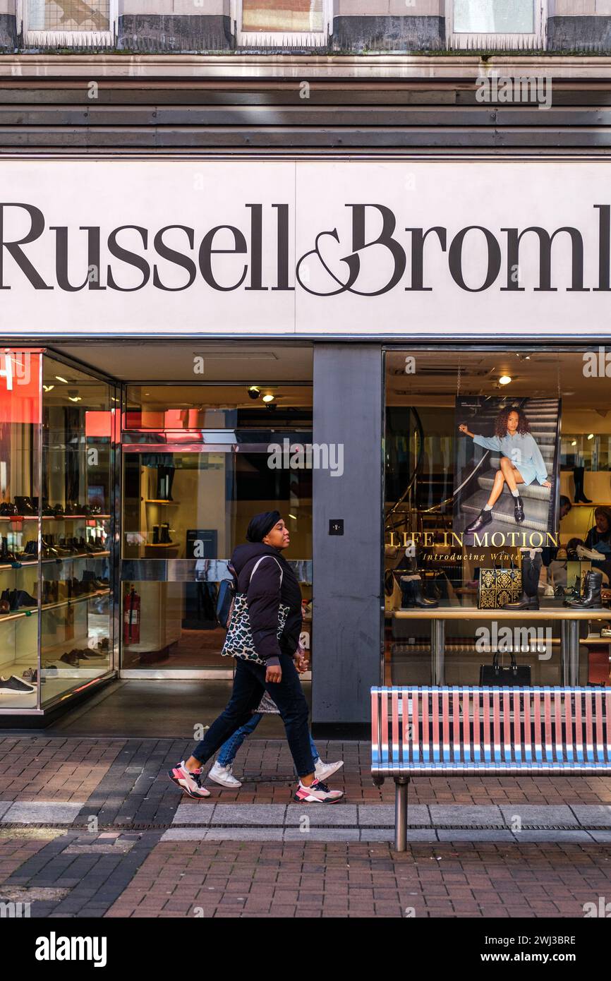 Kingston-Upon-Thames, London UK, February 12 2024, Woman Walking Past a High Street Branch Of Russell And Bromley High End Shoe Shop Retail Outlet Stock Photo
