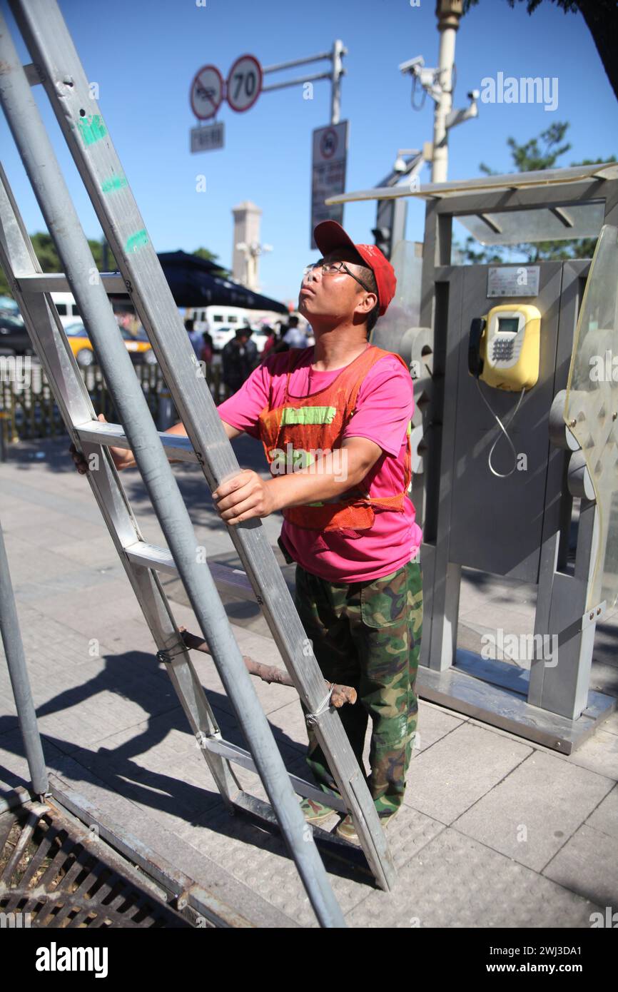 Chinese worker prepares to climb up the ladder to fix electric wire on July day 2015 in the capital of Beijing Stock Photo