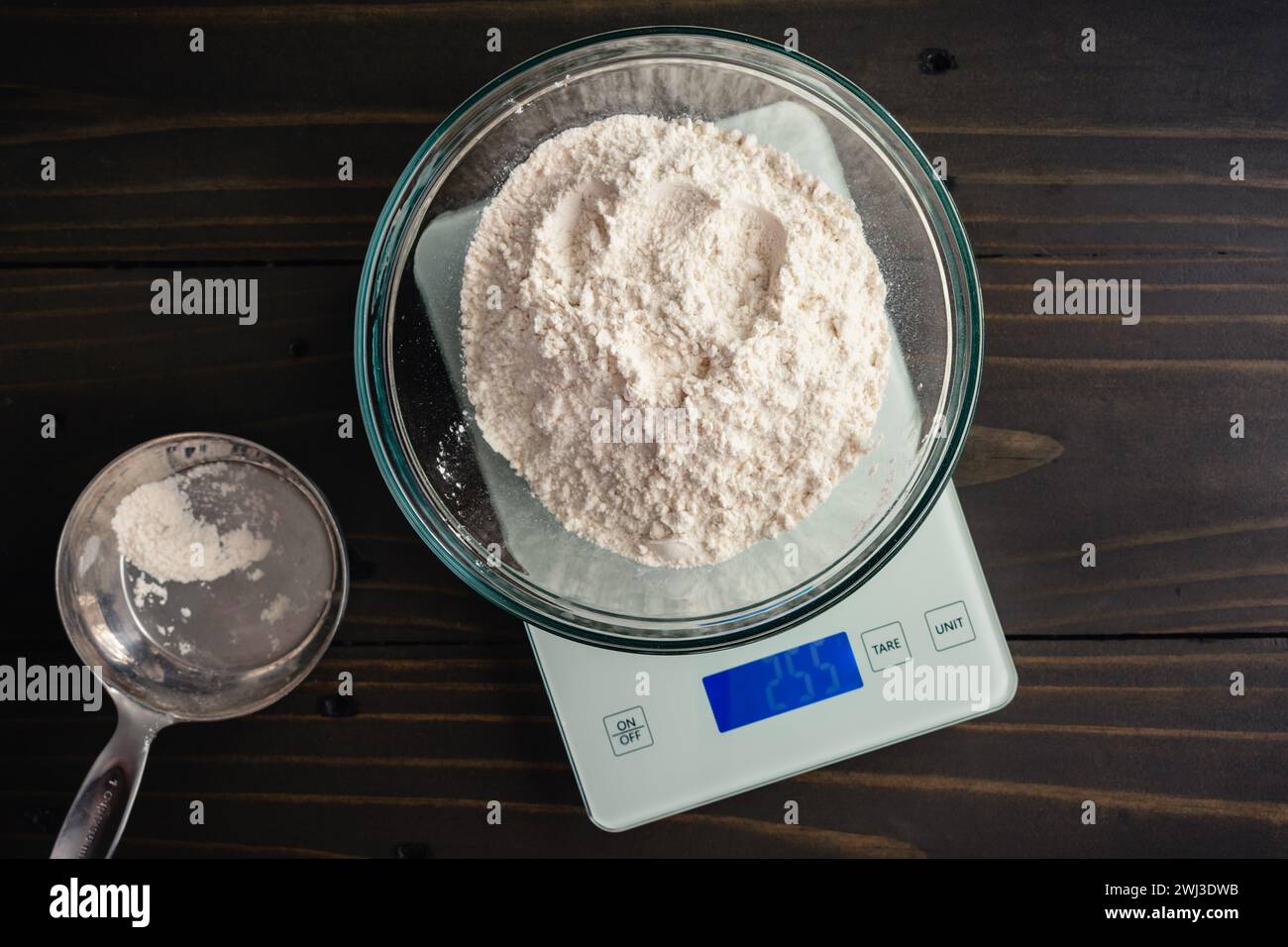 Weighing a Large Bowl of All-Purpose Flour on a Kitchen Scale: Glass mixing bowl of flour on a digital scale with a measuring cup on the side Stock Photo
