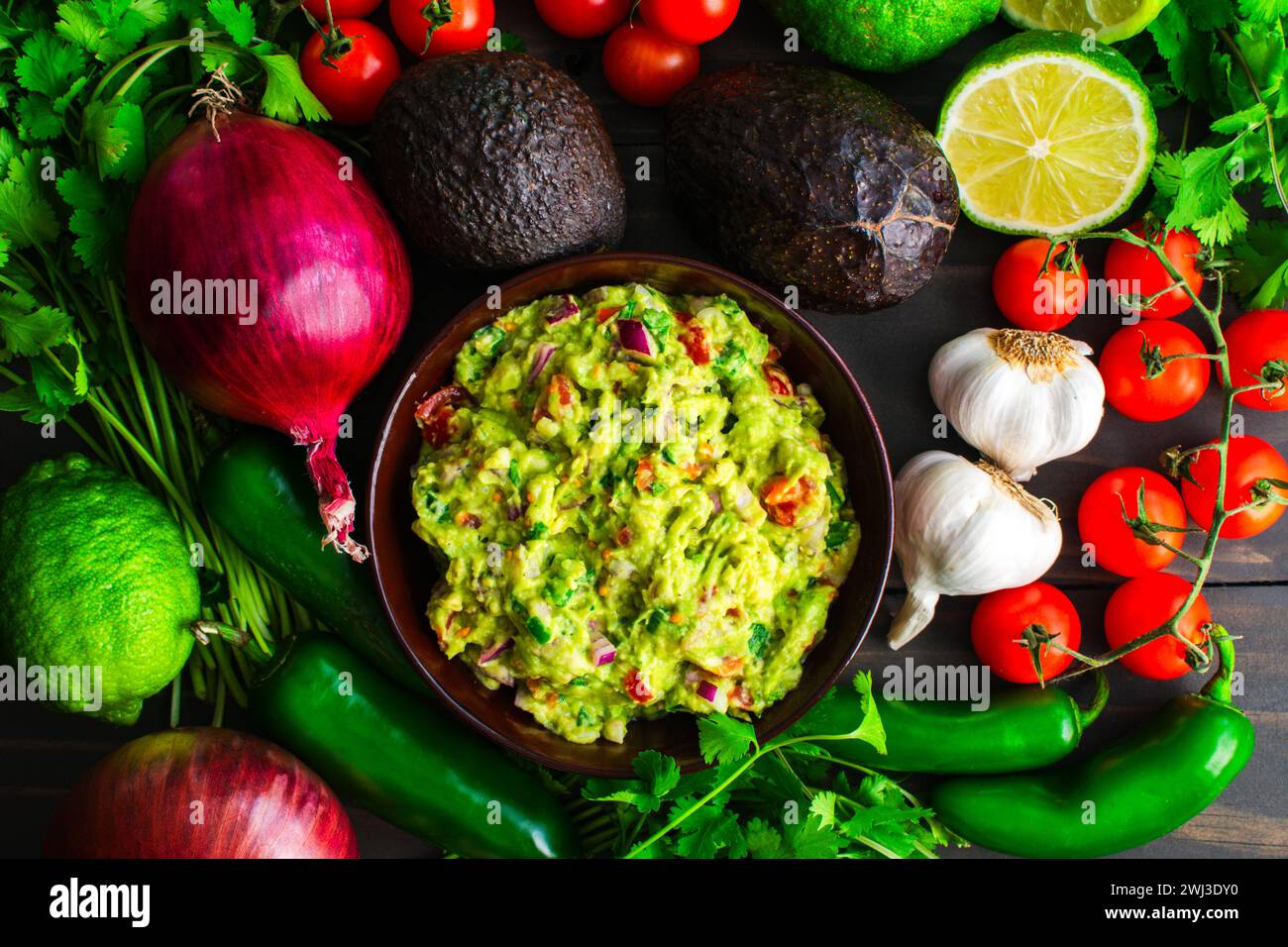 Bowl of Guacamole Surrounded by Fresh Ingredients: Guacamole with Hass avocados, jalapeno peppers, cherry tomatoes, and other ingredients Stock Photo