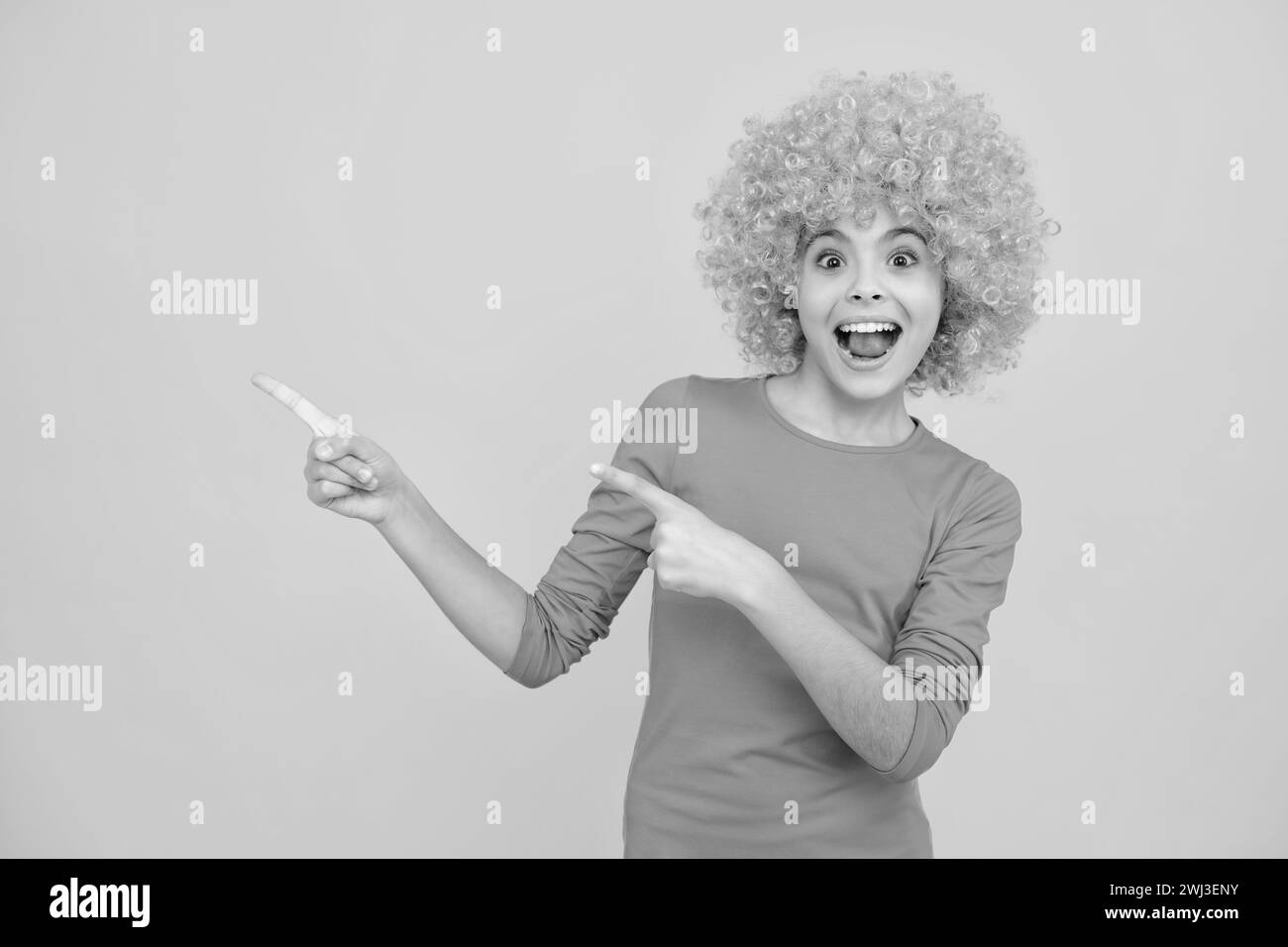 Girl with yellow wig. Funny child wearing orange curly wig hair, summer fun. Excited teenager, glad amazed and overjoyed emotions. Stock Photo