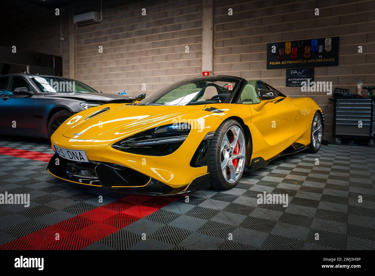 Yellow McLaren 765LT parked inside a Tuning Garage, on a Checkered Floor. Stock Photo