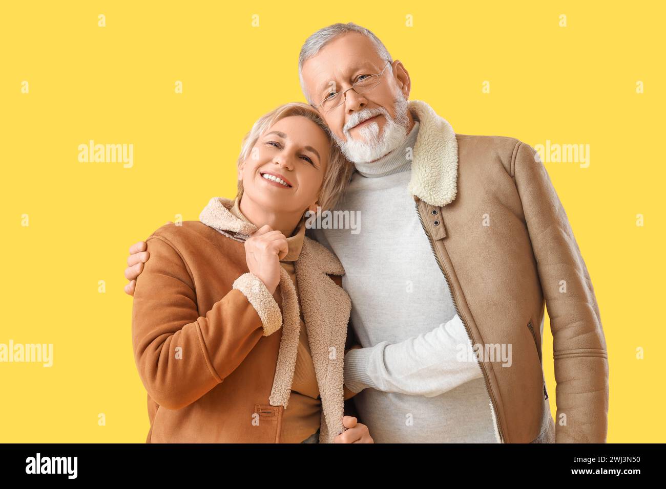 Mature couple in sheepskin coats hugging on yellow background Stock Photo