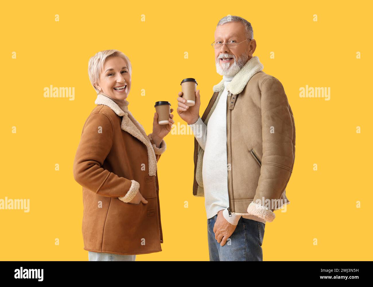 Mature couple in sheepskin coats with coffee cups on yellow background Stock Photo
