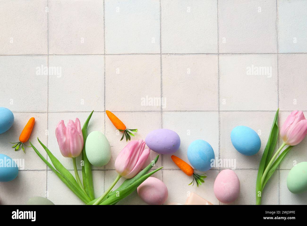 Painted Easter eggs with tulip flowers and carrots on white tile ...