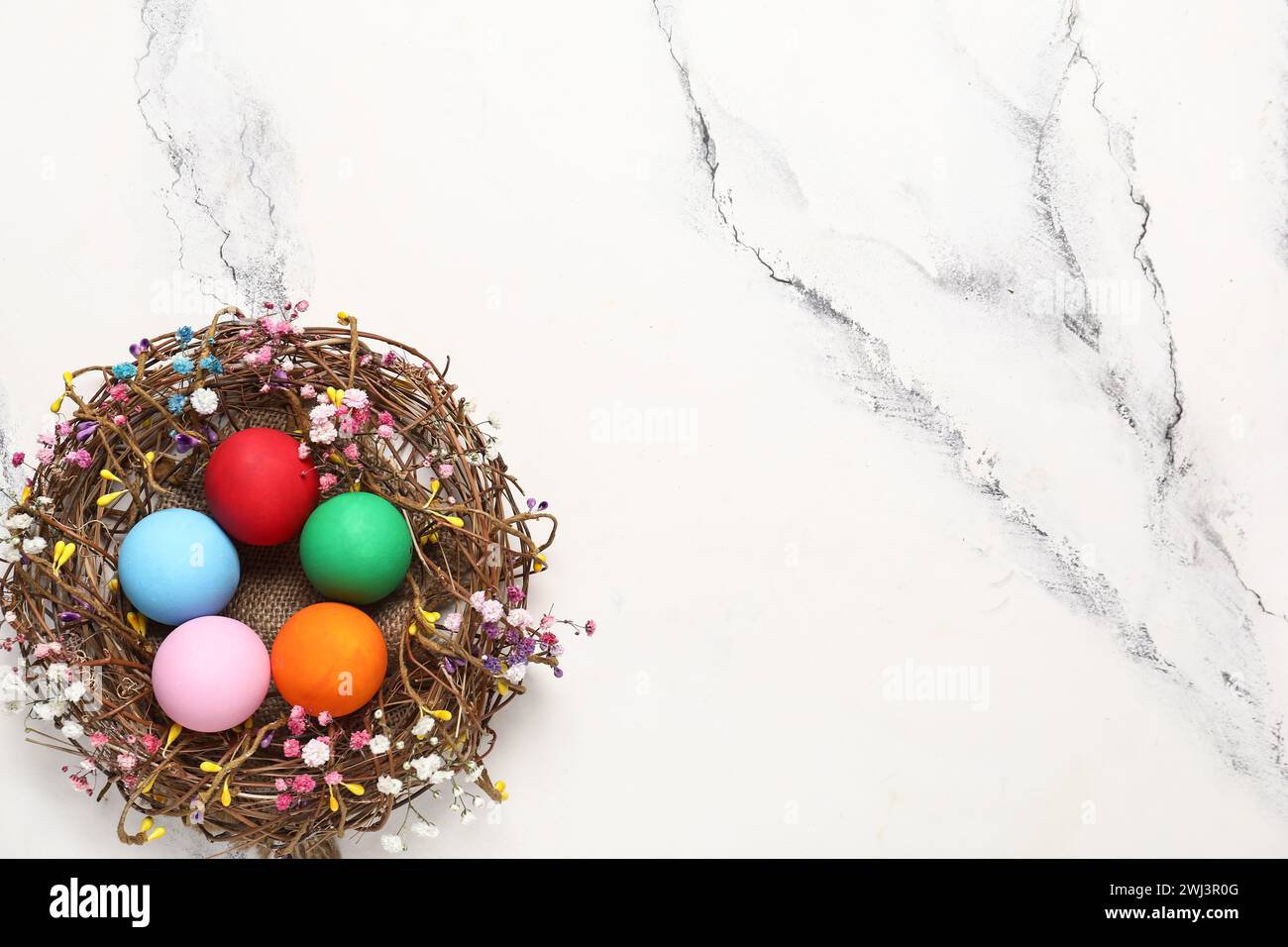 Wicker nest with painted Easter eggs and gypsophila flowers on light ...