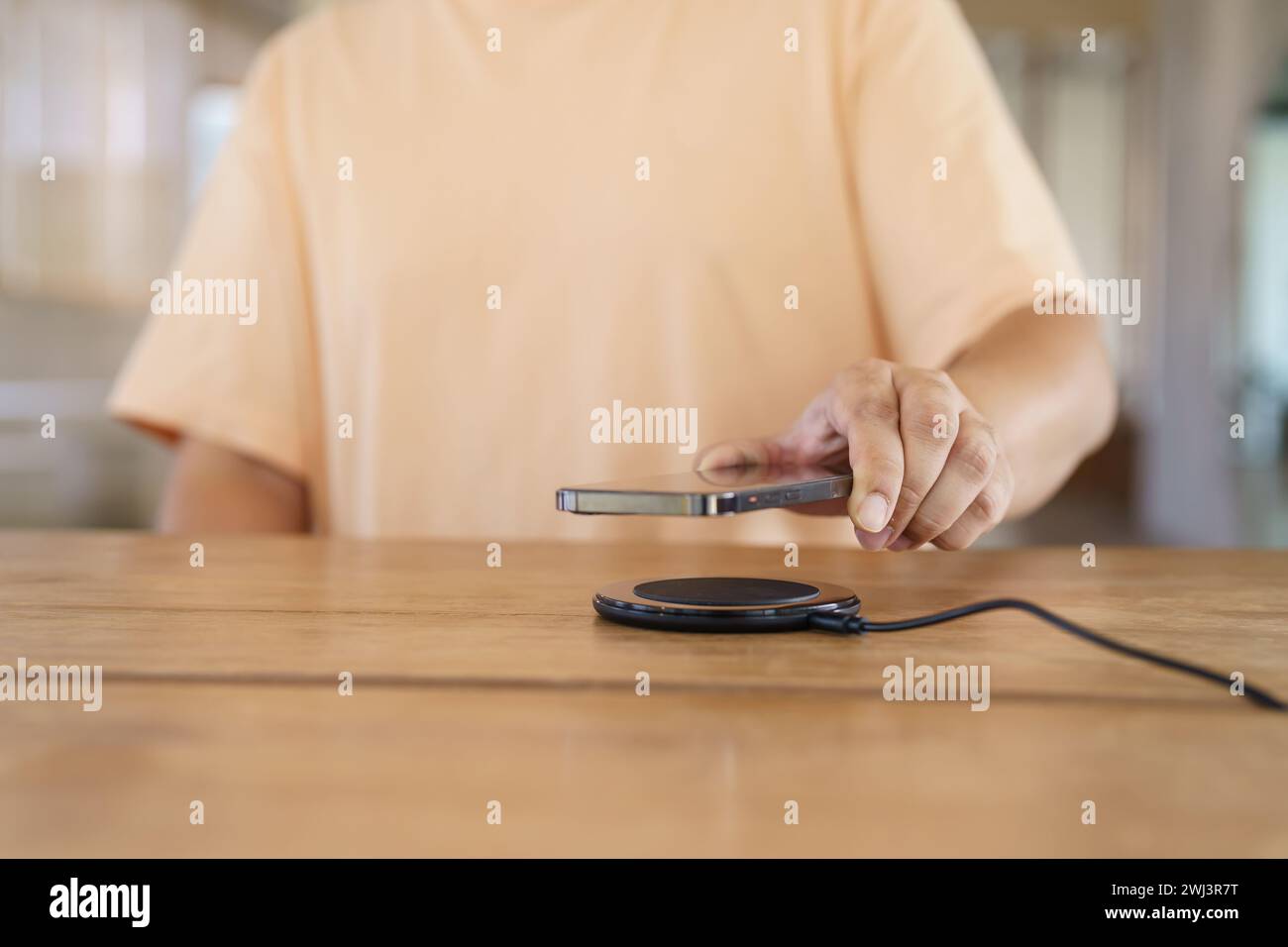 Charging mobile phone battery with wireless charging device in the table. Smartphone charging on a charging pad. Mobile phone ne Stock Photo