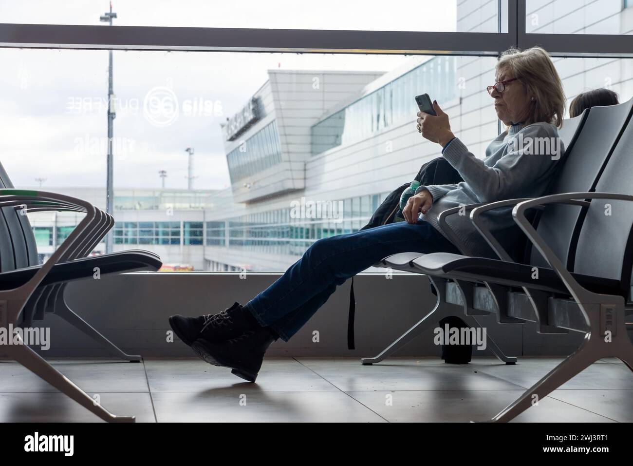 PRAGUE, CZECHIA, FEB 01 2024, Elderly woman looking at mobile phone while waiting at airport Stock Photo