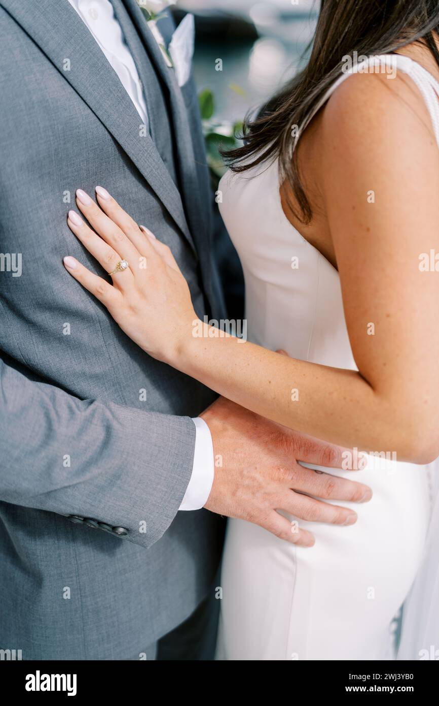 Groom hugs bride by the waist while standing on the street. Cropped. Faceless Stock Photo