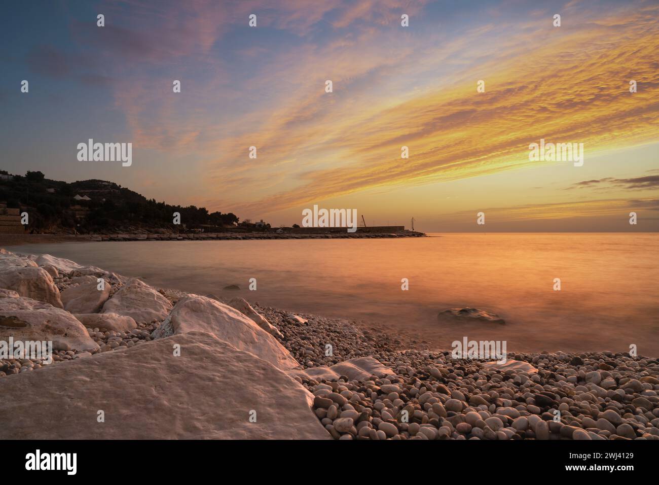 Colourful sunrise over the white pebble beach and harbor of Mattinata in Italy Stock Photo