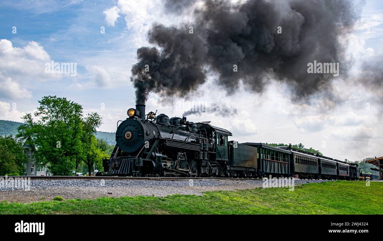 View of a Narrow Gauge Restored Steam Passenger Train Blowing Smoke, Starting To Pull Out of Station Stock Photo