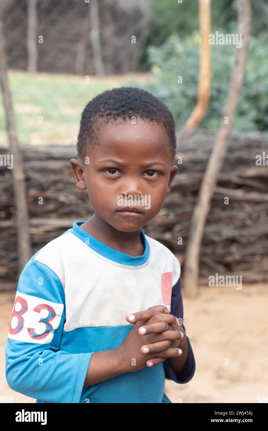 village african child portrait, standing outside in the yard, wattle wooden fence in the background Stock Photo