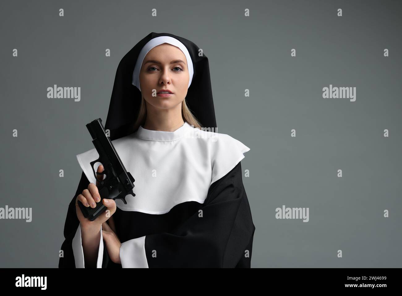 Woman in nun habit holding handgun on grey background. Space for text Stock Photo