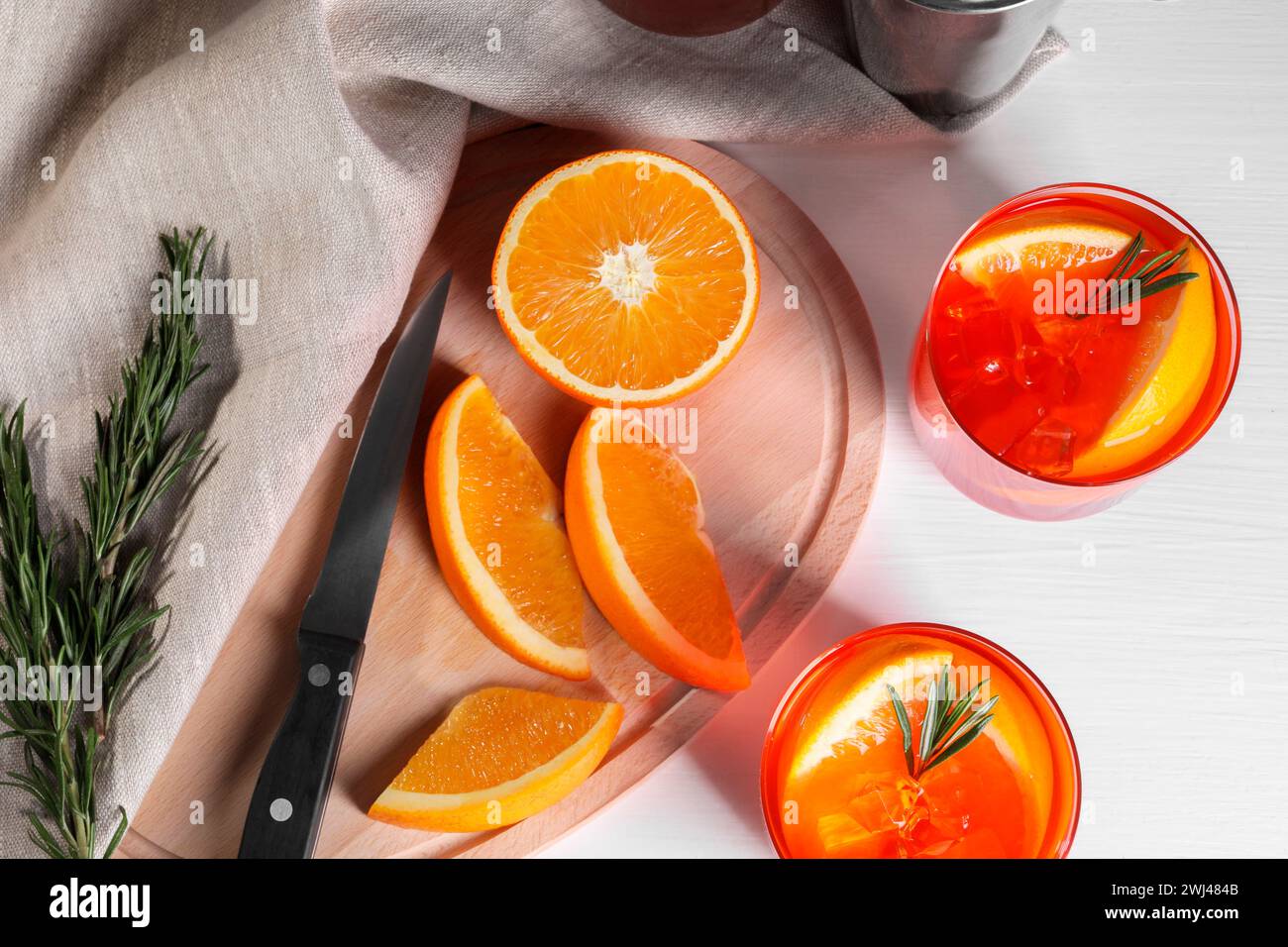 Aperol spritz cocktail, rosemary and orange slices on white table, flat ...