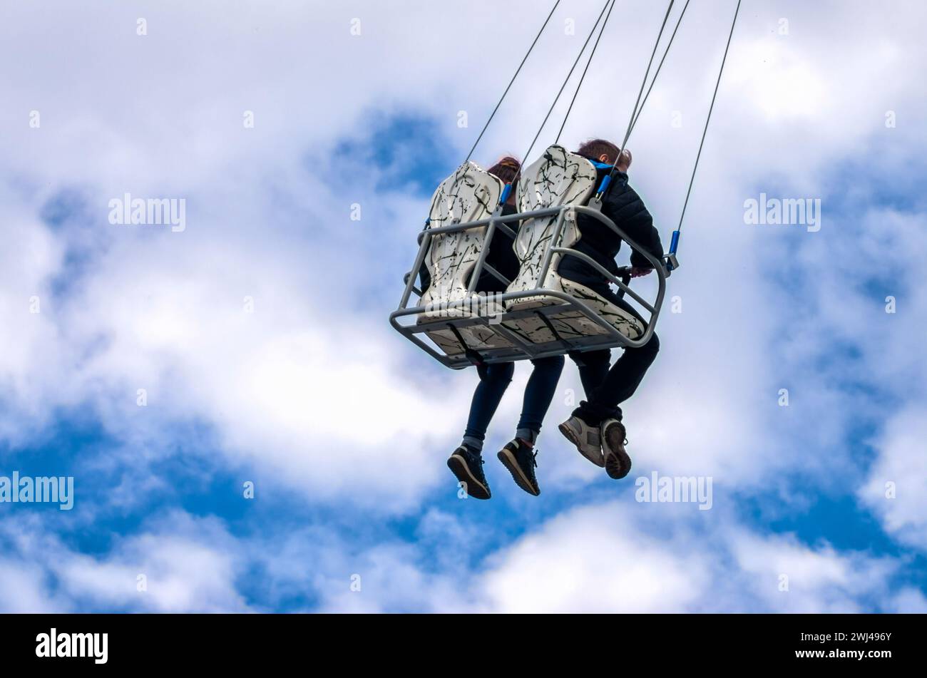 Children ride on a carousen on a background of blue sky and white clouds Stock Photo