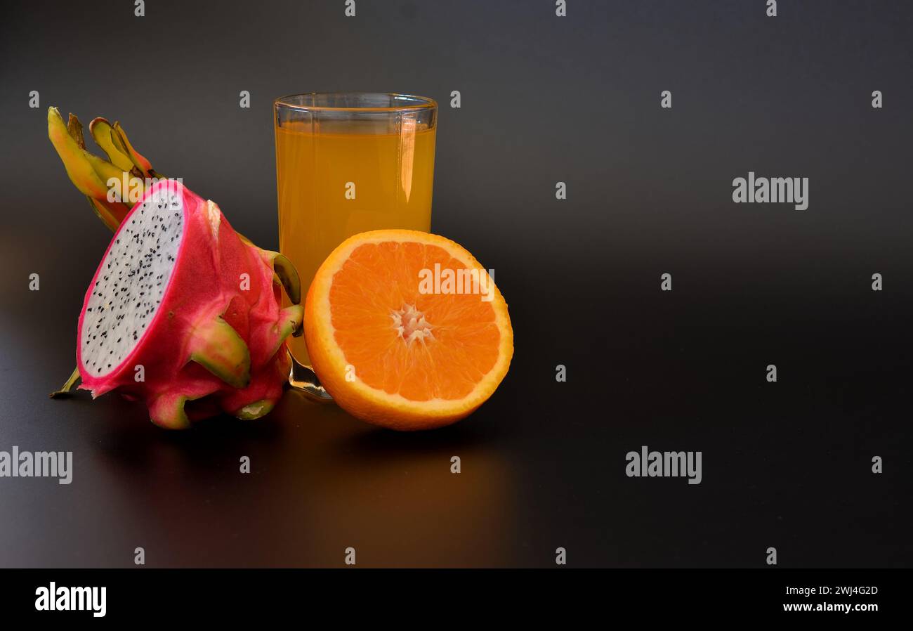 A tall glass of freshly squeezed fruit juice on a black background, next to half a ripe orange and pitaya. Close-up. Stock Photo
