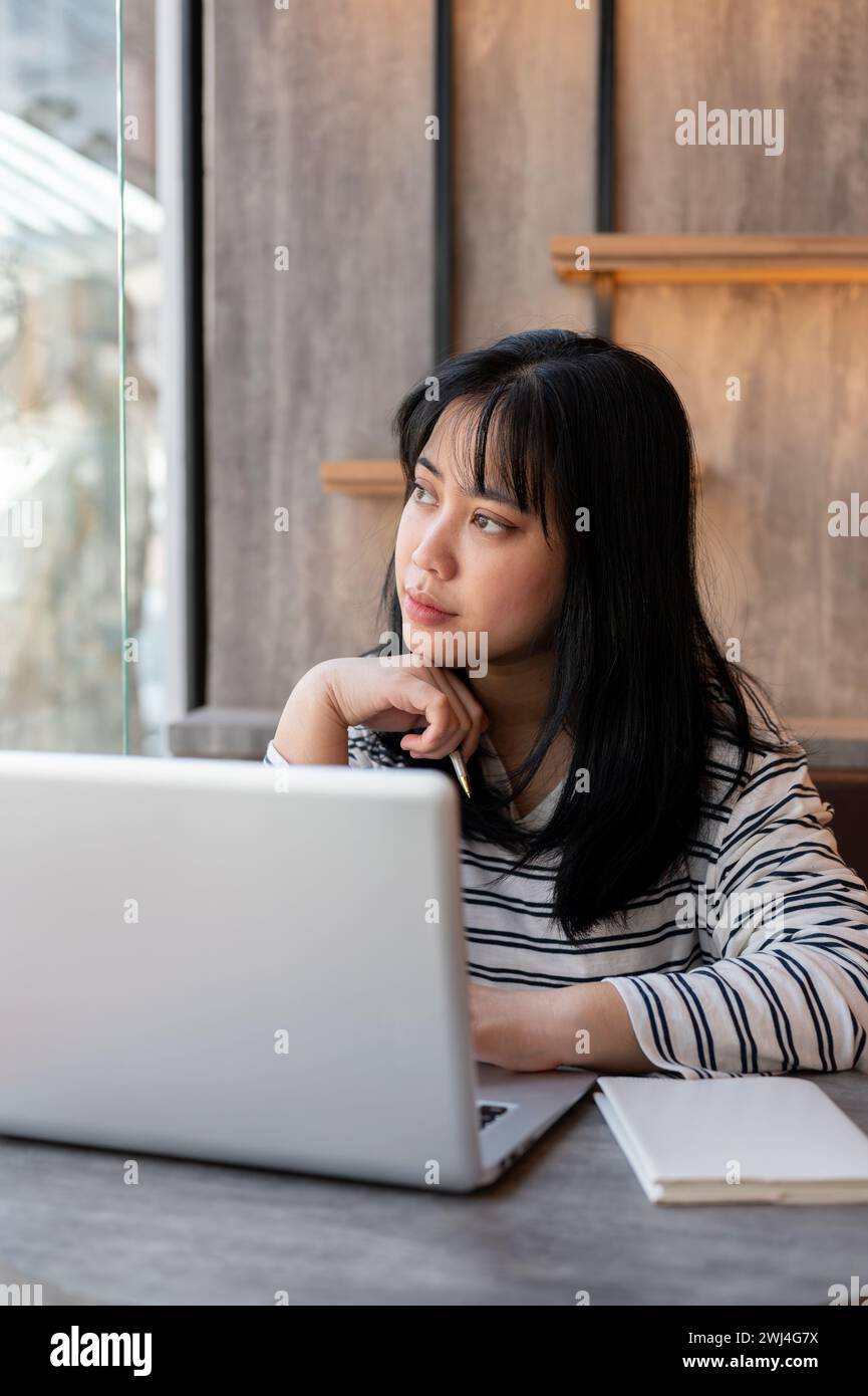 A serious, thoughtful Asian woman is looking out the window and ...
