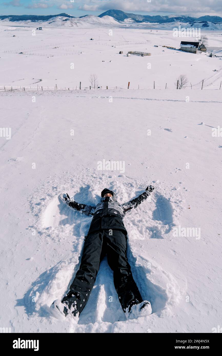 Young woman in a ski suit makes a snow angel in the snow Stock Photo