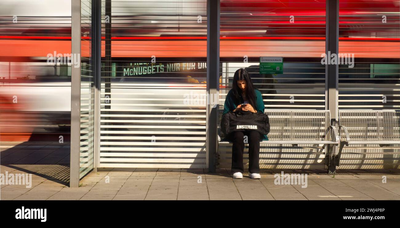 Young woman sitting on the platform and looking at her cell phone, main station, Giessen, Germany Stock Photo