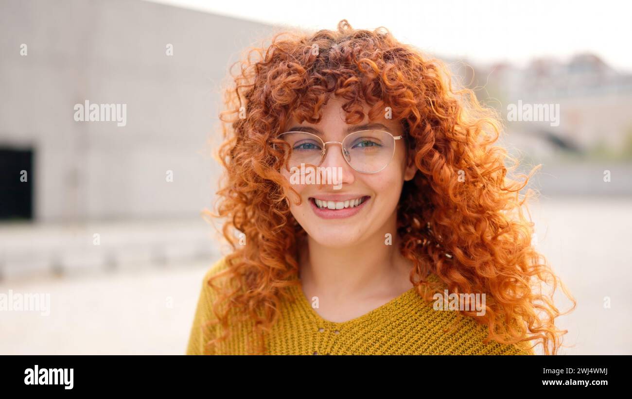 Redhead woman with curly long hair smiling at camera Stock Photo