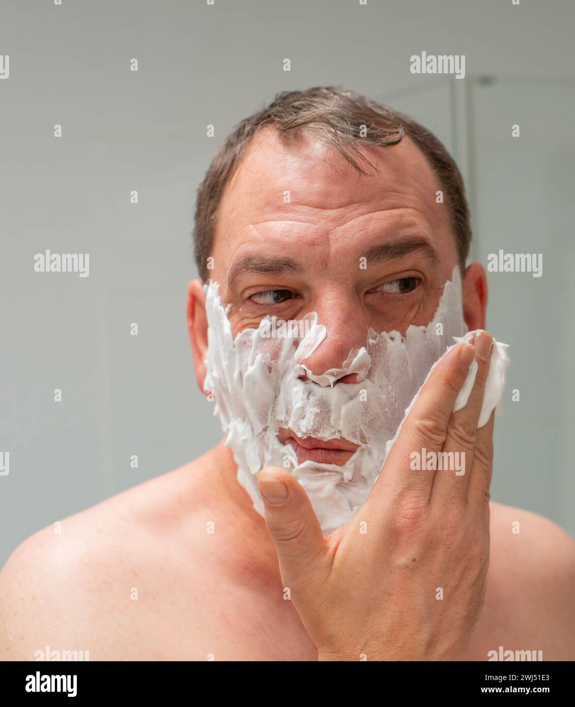 Male in front of a mirror while shaving a beard and facial care Stock Photo