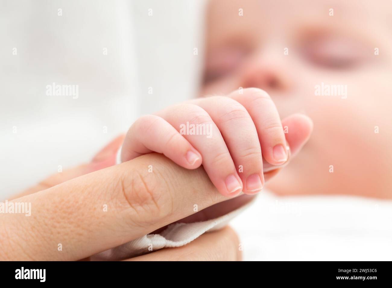 Newborn's tiny hand clutches mother's finger. Concept of maternal bond and love Stock Photo