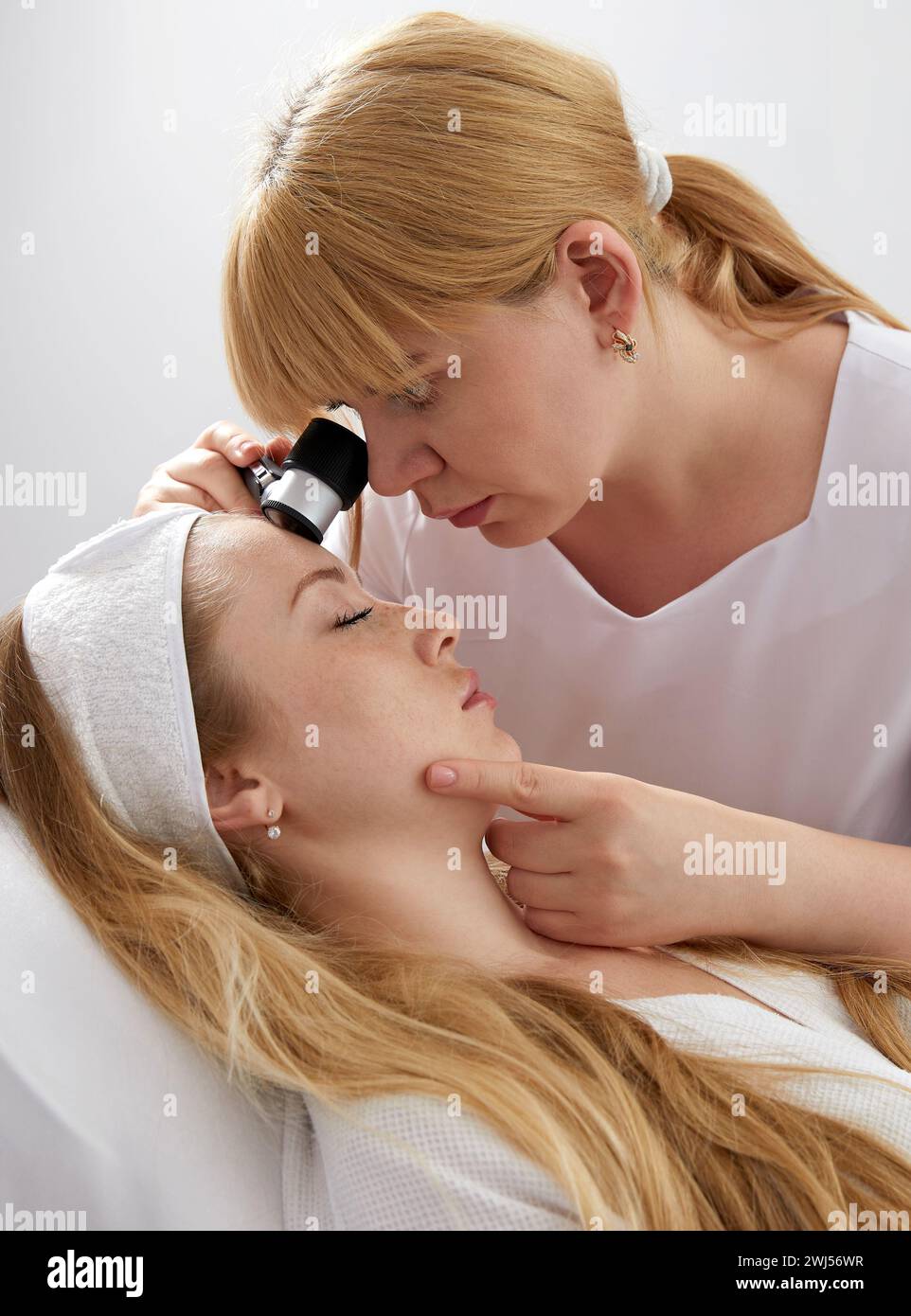 Woman gets professional skin exam at doctor's office. Dermatologist or cosmetology specialist uses magnifying glass to investiga Stock Photo