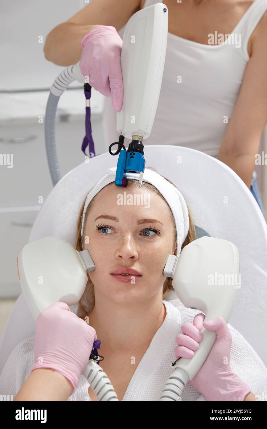 Conceptual beauty and cosmetology image of hands of several doctors holding laser equipment over female face. Beauty and Cosmeto Stock Photo