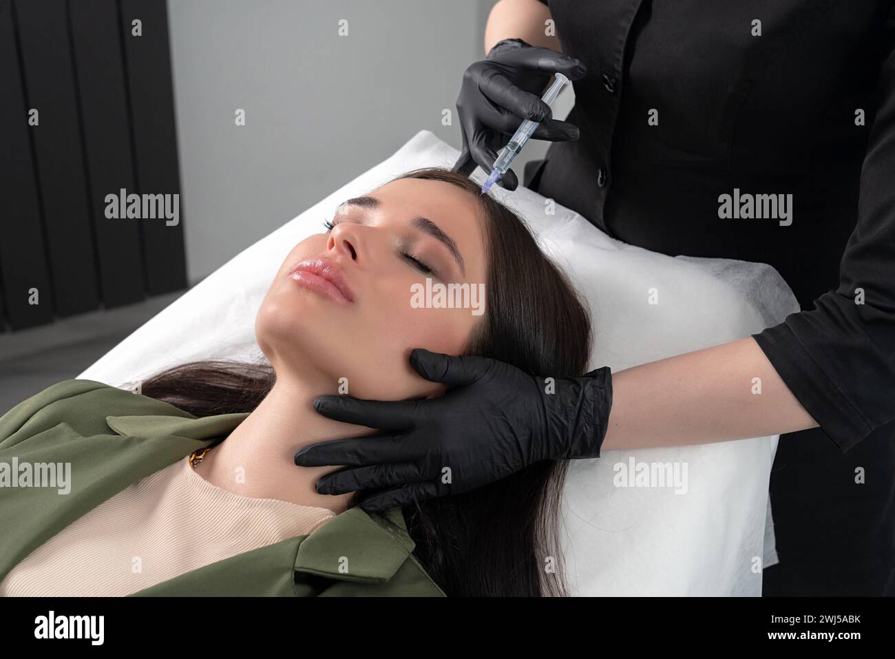 Young woman with hair problem receiving injection in head skin in a clinic. Mesotherapy treatment of hair loss, injection for ha Stock Photo
