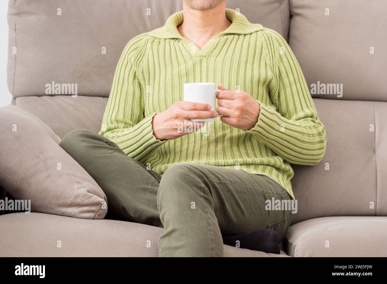 Front view of a legs of a man holding a cup of coffee in winter sitting on a couch in the living room at home Stock Photo