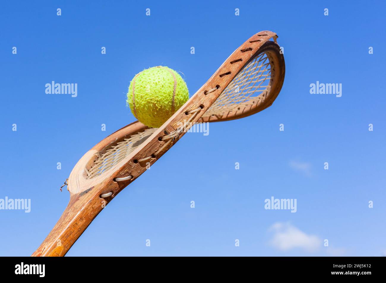 Old Tennis Racket Bent Twisted Frame with Ball attached closeup blue