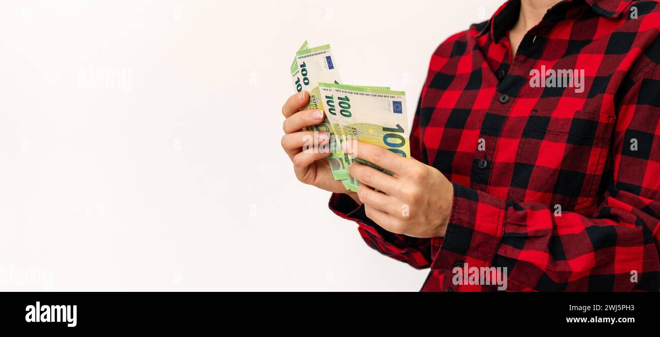 Female person counts euro notes in her hands in front of plain background. Money transfer. Savings and social payments. Stock Photo