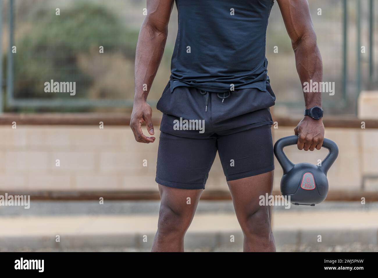 Crop anonymous black male athlete in tight sportswear holding heavy kettlebell while training on sports ground in city Stock Photo