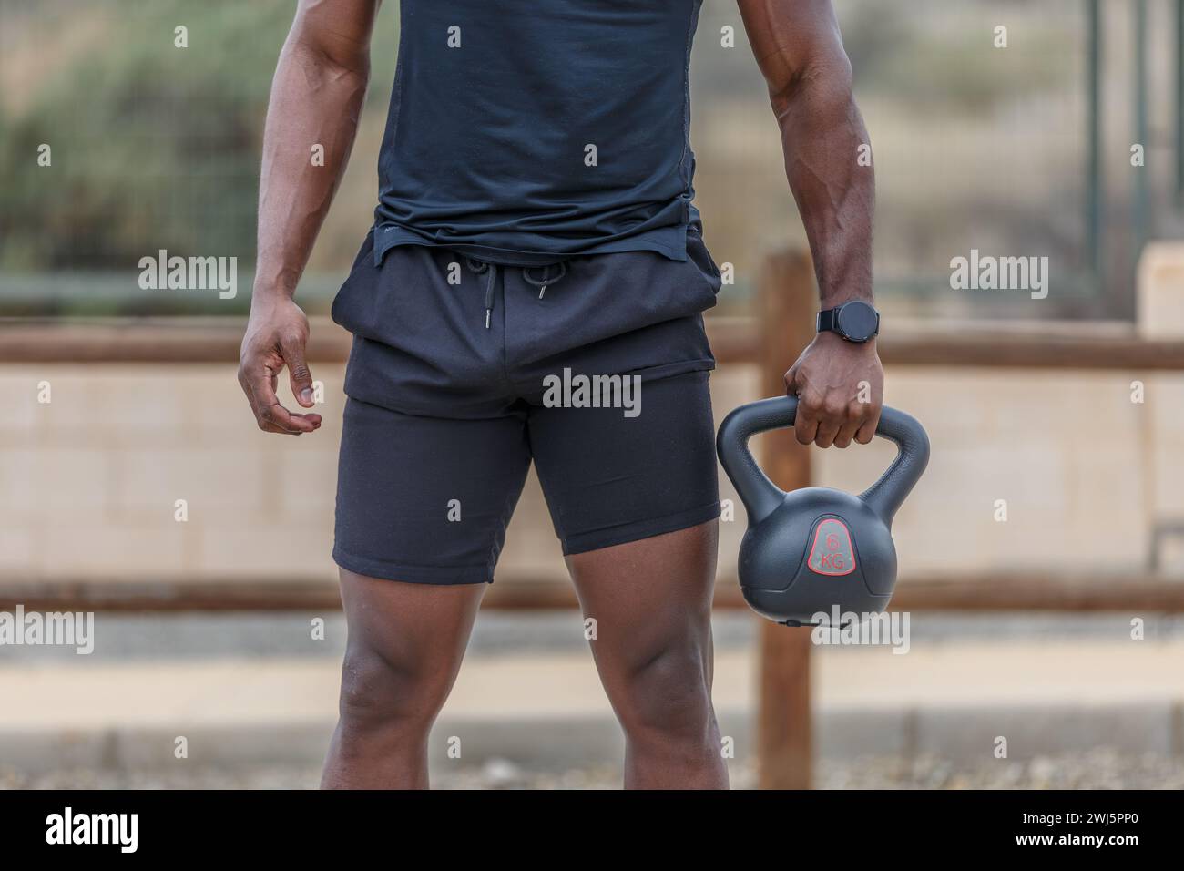 Crop anonymous African American athlete with sportive muscular body wearing tight black sportswear holding heavy kettlebell during intense weightlifti Stock Photo