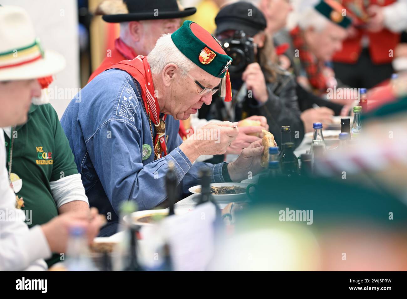 Riedlingen, Germany. 13th Feb, 2024. Winfried Kretschmann, Minister President of Baden-Württemberg (center, The Greens/Alliance 90, M), eats a plate of frog tripe in the town hall on Shrove Tuesday. More than 300 jesters from the Gole 1865 jesters' guild take part in the cigar smoking, the 193rd frog tripe eating and the subsequent slide out of the town hall and later want to gamble through the city. Froschkutteln is a Riedlingen specialty. It consists of sliced beef stomach marinated in vinegar. Credit: Felix Kästle/dpa/Alamy Live News Stock Photo