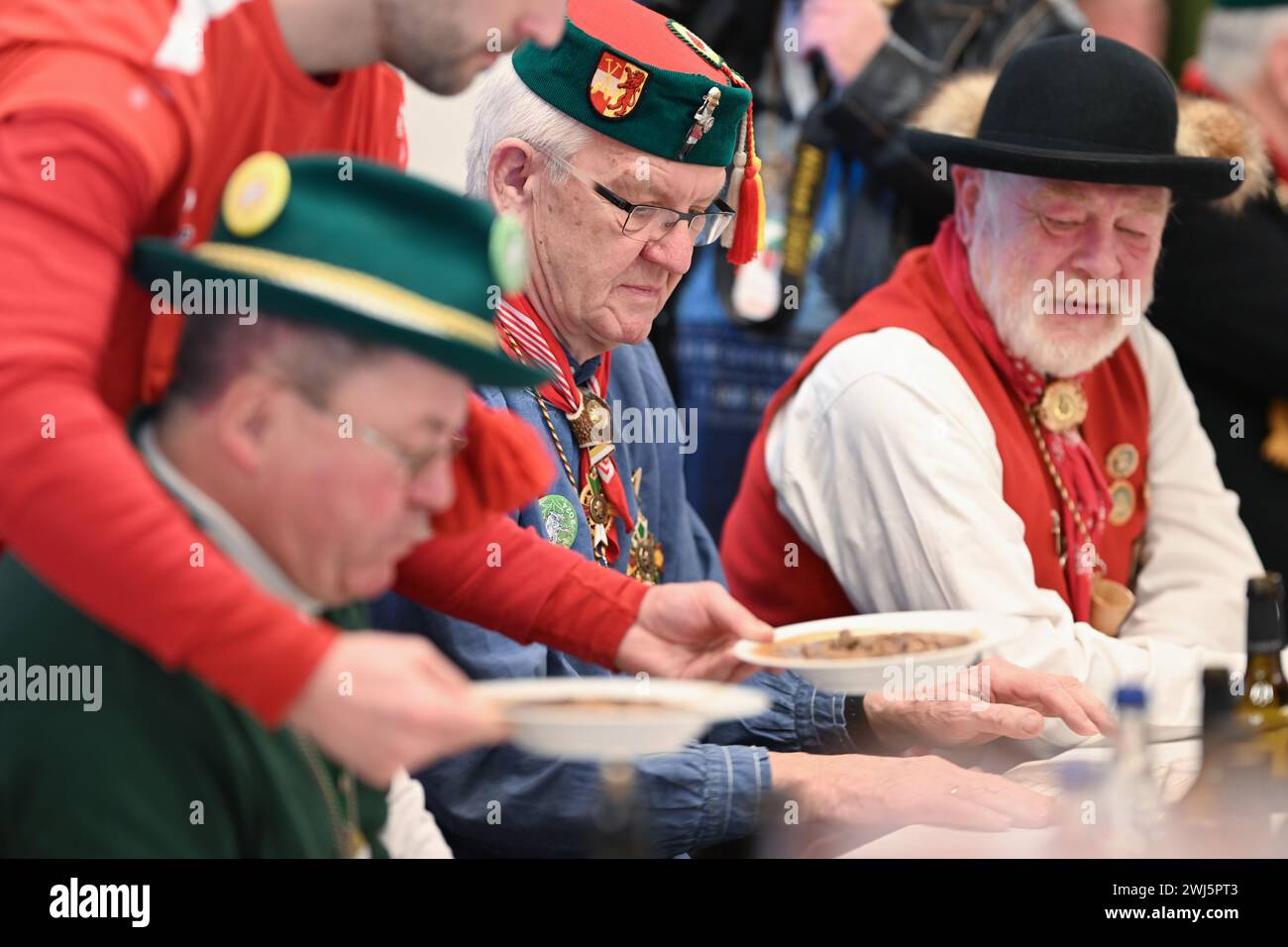 Riedlingen, Germany. 13th Feb, 2024. Winfried Kretschmann, Minister President of Baden-Württemberg (center, The Greens/Alliance 90, M), is served a plate of frog tripe at the town hall on Shrove Tuesday. More than 300 jesters from the Gole 1865 jesters' guild take part in the cigar smoking, the 193rd Froschkuttel meal and the subsequent slide out of the town hall and later want to gamble through the city. Froschkutteln is a Riedlingen specialty. It consists of sliced beef stomach marinated in vinegar. Credit: Felix Kästle/dpa/Alamy Live News Stock Photo