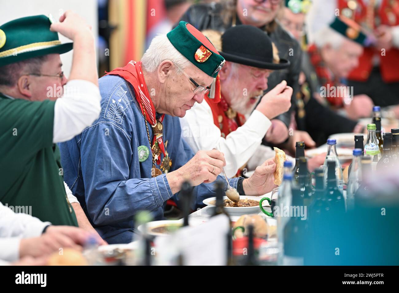 Riedlingen, Germany. 13th Feb, 2024. Winfried Kretschmann, Minister President of Baden-Württemberg (center, The Greens/Alliance 90, M), eats a plate of frog tripe in the town hall on Shrove Tuesday. More than 300 jesters from the Gole 1865 jesters' guild take part in the cigar smoking, the 193rd frog tripe eating and the subsequent slide out of the town hall and later want to gamble through the city. Froschkutteln is a Riedlingen specialty. It consists of sliced beef stomach marinated in vinegar. Credit: Felix Kästle/dpa/Alamy Live News Stock Photo