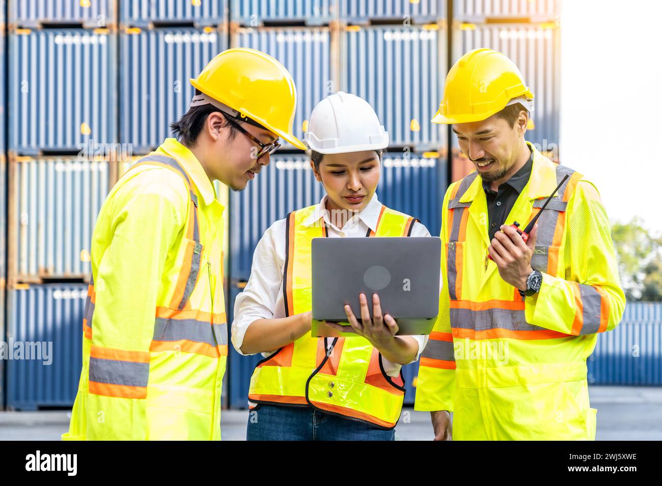 A female worker and two male workers wearing yellow safety vests using a laptop. Stock Photo
