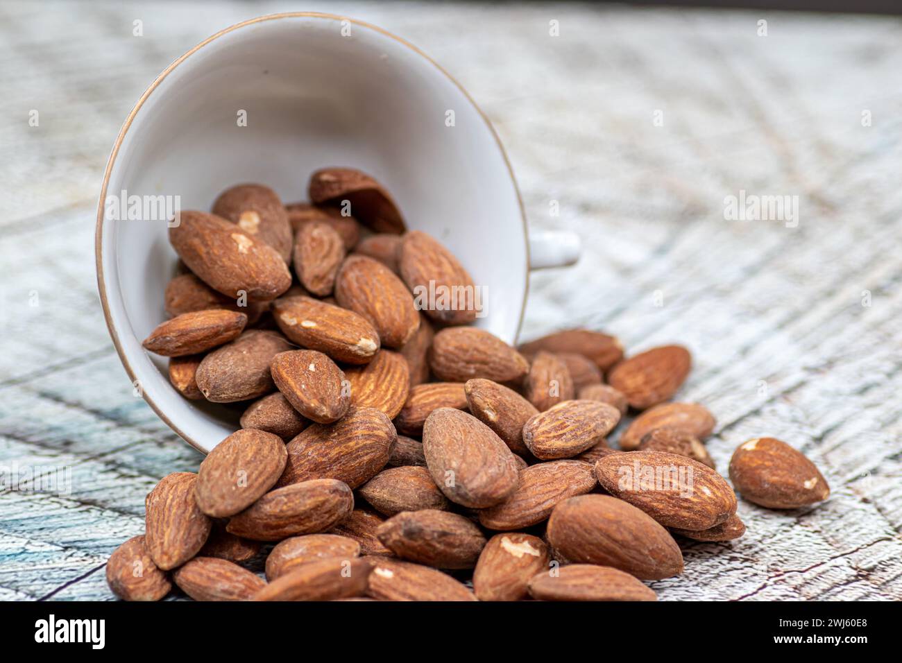 Close up roasted organic brown almond seed on wooden table and some of almond in white porcelain cup Stock Photo