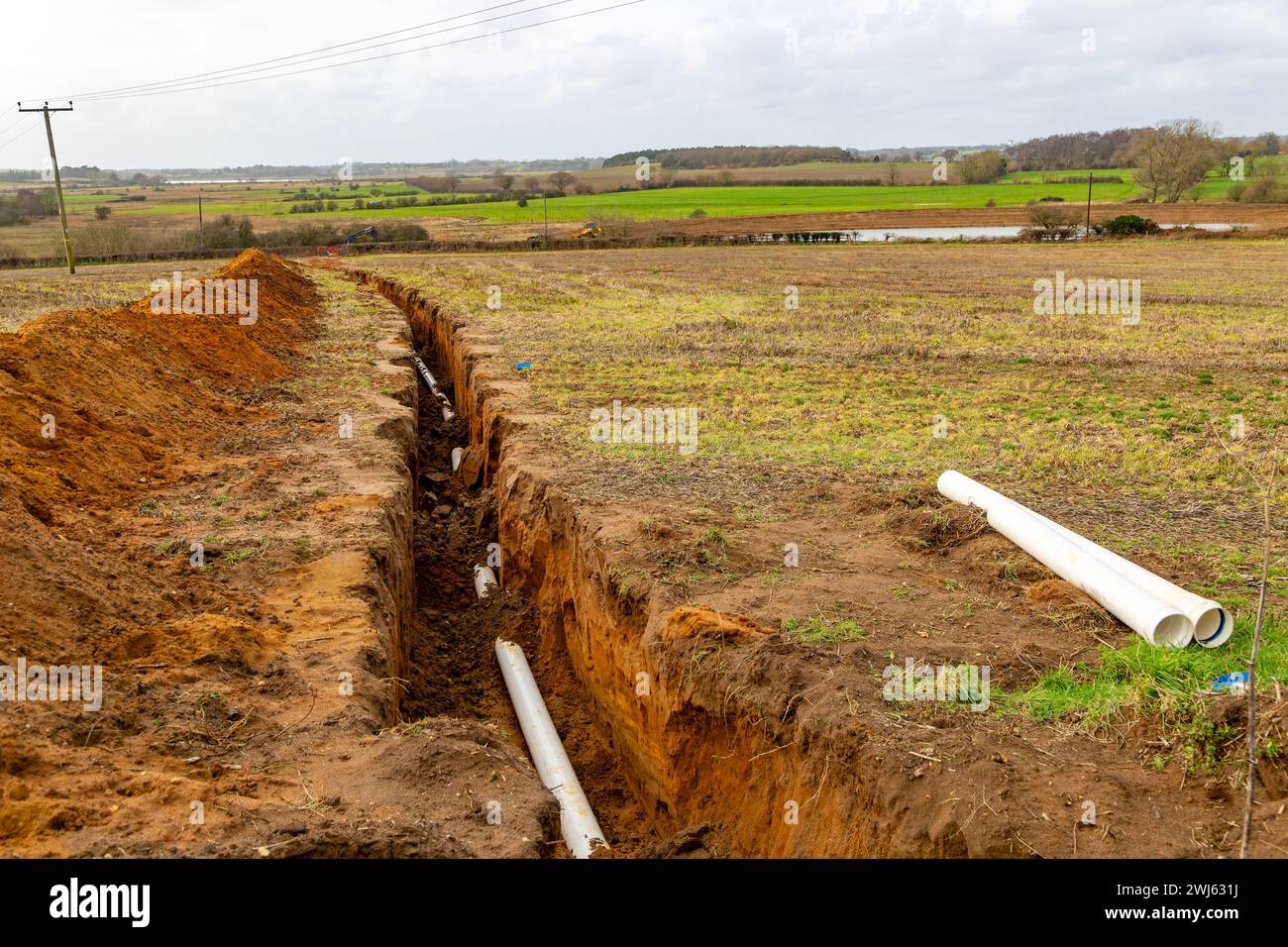 Farm irrigation water supply pipeline excavated in ditch in sandy soil, Shottisham, Suffolk, England, UK reservoir in distance Stock Photo