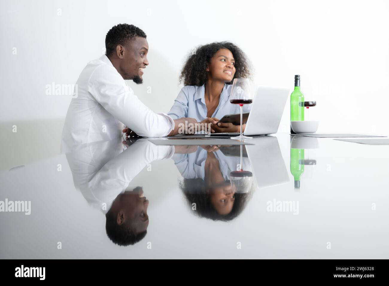 Both of young businesses drinking wine and use their laptops to share information with each other in their living room of house. Stock Photo