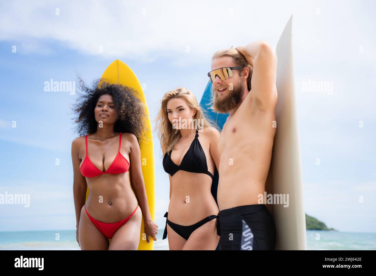 Group of friends in swimsuits posing with surfboards on the beach. Stock Photo