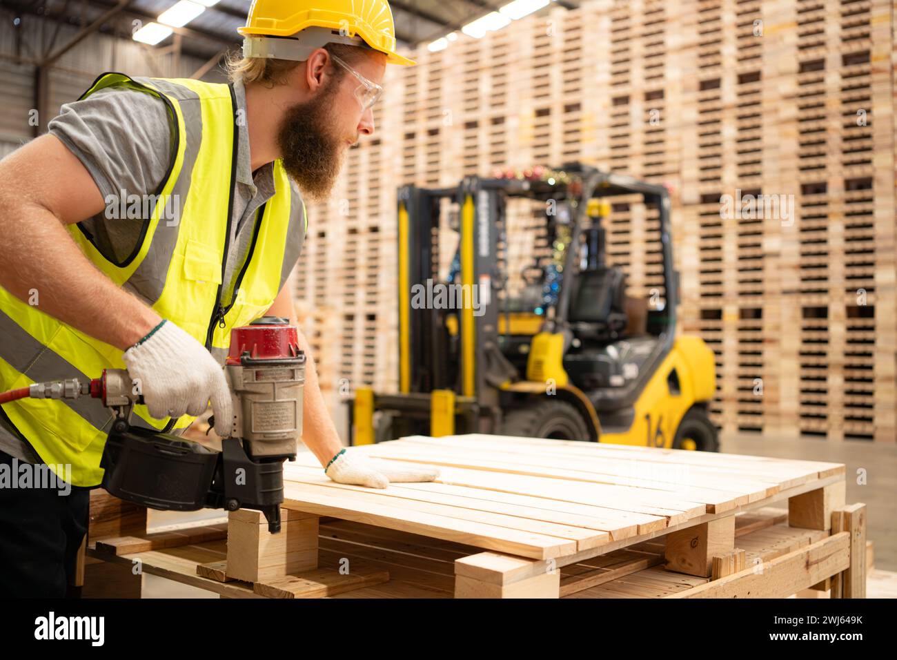 Young workers working in a woodworking factory, Using a nailing machine to assemble wooden pallets Stock Photo