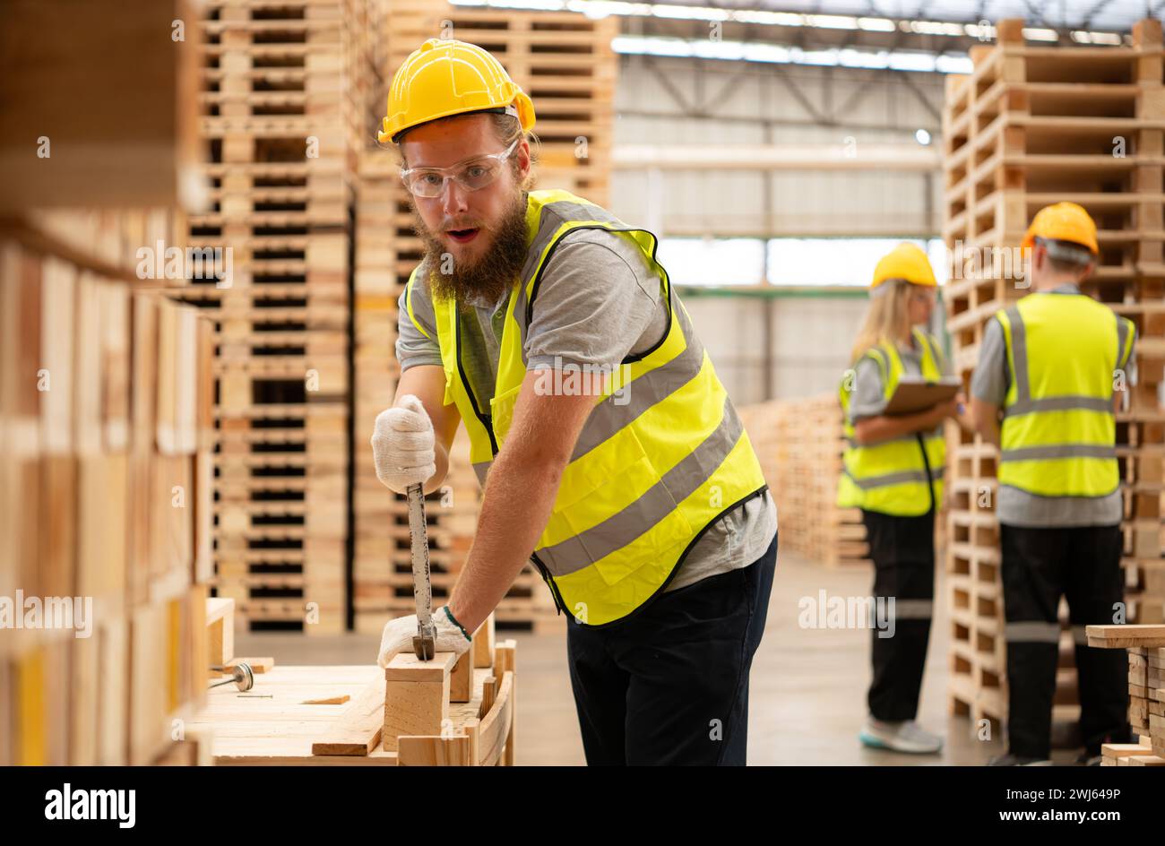 Young workers working in a woodworking factory, Using a hammer to work assembling pallet parts Stock Photo