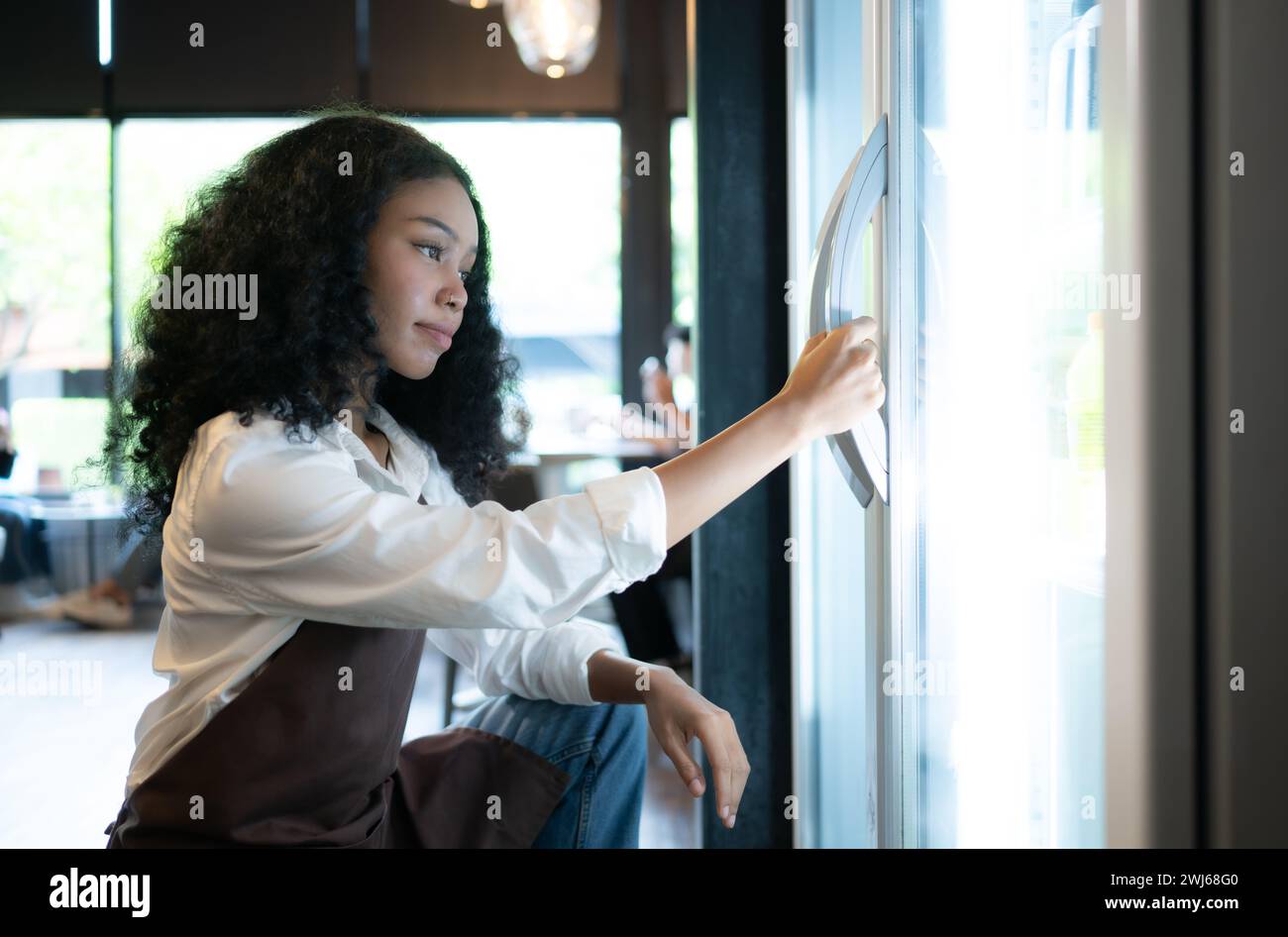 The owner of a coffee shop looks inside the refrigerator to retrieve chilled food to serve a customer. Stock Photo